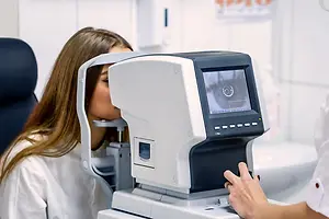 A woman is getting her eyes examined using a machine by a medical professional