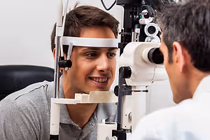 A man is looking into an eye examination machine while the doctor is checking his eye with a device in the clinic