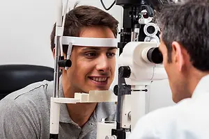 A man is looking into an eye examination machine while the doctor is checking his eye with a device in the clinic