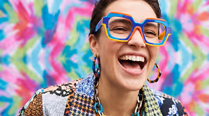 A young woman in a colorful jacket and sunglasses is smiling for the camera.