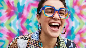 A young woman in a colorful jacket and sunglasses is smiling for the camera.