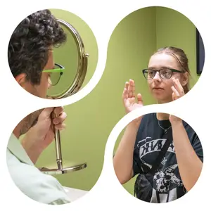 A person is looking at their face in a mirror while another person holds the mirror. The other person is looking at their face and holding their hands together. A girl with a backpack is also looking at their face. The room is painted green. The image is circular and has a white border.