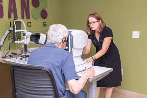 A woman is examining an older man's eyes using a machine in an eye clinic.