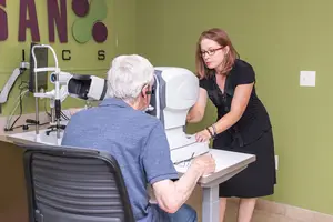 A woman is examining an older man's eyes using a machine in an eye clinic.