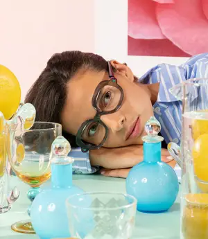 A woman with glasses resting her head on a table with blue vases and glasses with lemons