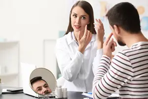 A female doctor talks to a male patient while looking in a mirror in an office