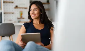 Woman sitting on the couch holding a tablet and smiling