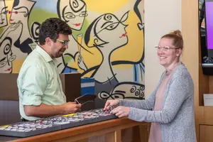 A man and a woman are standing in front of a desk with eyeglasses on top and smiling at each other.