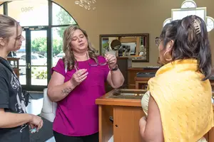Three women stand inside a jewelry store with one woman examining a pair of eyeglasses