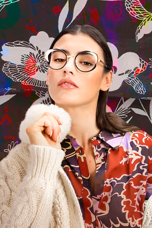 A woman wearing glasses is posing for a photo with a floral background