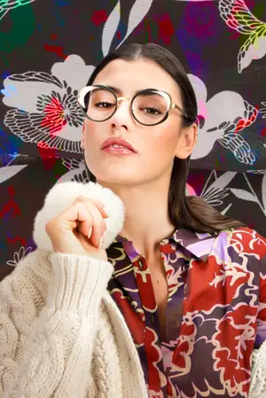A woman wearing glasses is posing for a photo with a floral background