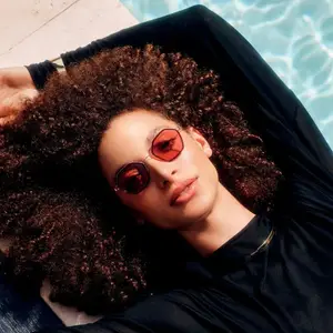 A woman with curly hair lying by the pool wearing sunglasses