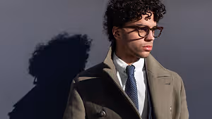 A man in a coat and tie standing against a wall with his shadow on the wall