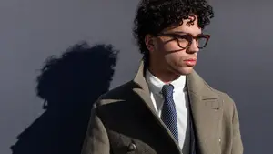 A man in a coat and tie standing against a wall with his shadow on the wall