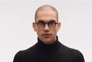 A bald man wearing a black turtleneck and glasses with a serious expression