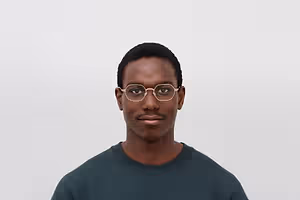 A man with glasses and a green shirt standing and smiling in front of a white background.