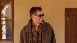 A man with sunglasses and a scarf standing against a yellow wall