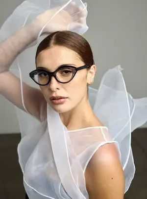 A woman in a transparent dress with a veil over her head, wearing glasses and posing for a photo.
