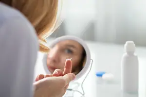 Woman putting on a contact lens and looking in the mirror