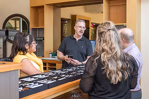 A man in a black polo shirt is standing behind a counter and talking to a group of people in front of him