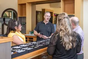 A man in a black polo shirt is standing behind a counter and talking to a group of people in front of him