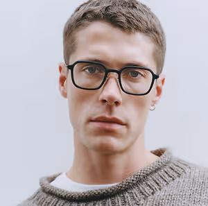A man wearing glasses and a sweater posing for a photograph