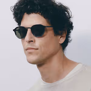 A man with curly hair wearing sunglasses and a white shirt