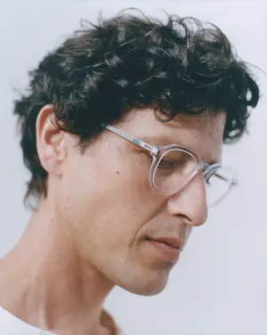 A close-up shot of a man with curly hair wearing glasses and looking down.
