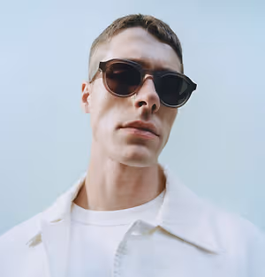 A man wearing sunglasses is standing against a blue background