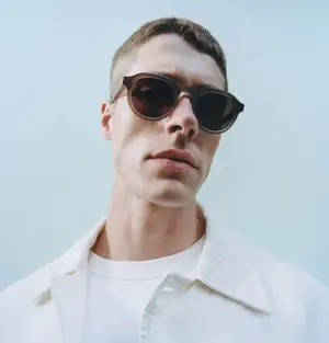 A man wearing sunglasses is standing against a blue background