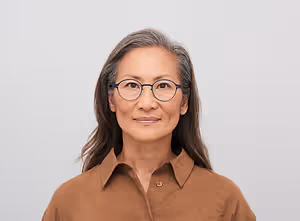Portrait of a woman wearing glasses and a brown shirt smiling at the camera