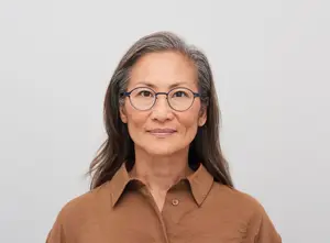 Portrait of a woman wearing glasses and a brown shirt smiling at the camera