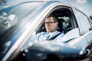 A man in a business suit drives a car in a parking lot