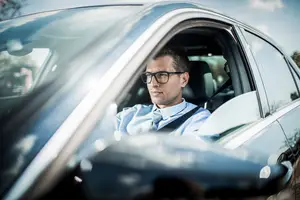 A man in a business suit drives a car in a parking lot