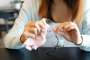 A woman is cleaning her eyeglasses with a pink cloth.