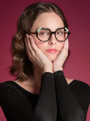 A woman wearing glasses and a black top posing with her hands on her face.