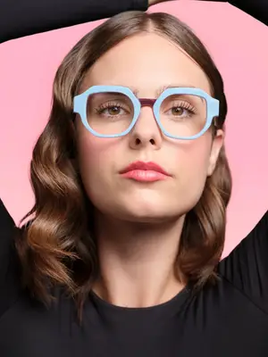 Woman with brown wavy hair wearing blue frame glasses posing for a photo