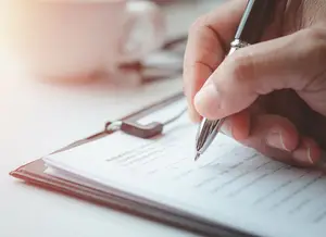 person holding a pen writing on a document