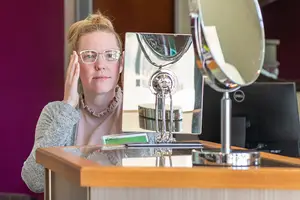 A woman sitting in front of a mirror wearing glasses and a necklace