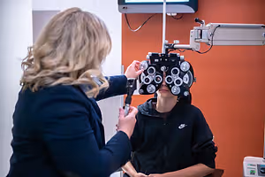 A woman doctor in a clinic room adjusting the eyepiece of an ophthalmoscope on a woman patient