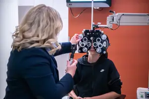 A woman doctor in a clinic room adjusting the eyepiece of an ophthalmoscope on a woman patient