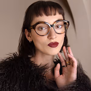 woman wearing glasses and rings in front of a beige wall