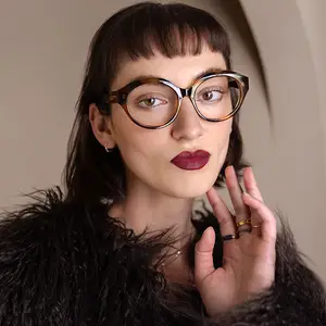 woman wearing glasses and rings in front of a beige wall
