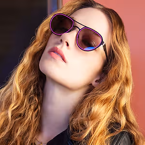 Woman with long wavy blonde hair wearing black leather jacket and purple framed sunglasses