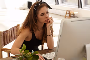 woman in a black sleeveless top wearing a polka-dot headband looking at a computer monitor with her left hand on her face