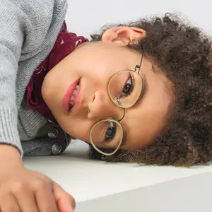 A young child wearing glasses with a gray sweater and a red scarf looks directly at the camera with a slightly surprised expression