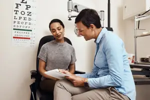 A doctor is talking to a patient while holding a paper and pen in his hand.