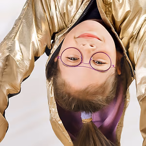 A girl wearing glasses and a gold jacket with her hair in a ponytail