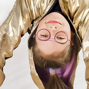 A girl wearing glasses and a gold jacket with her hair in a ponytail