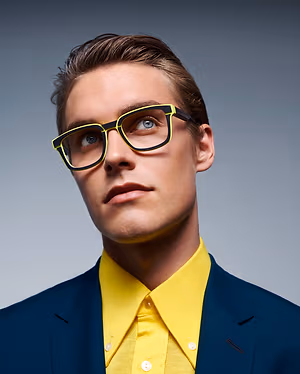 A man with brown hair wearing yellow glasses and a yellow shirt and blue blazer
